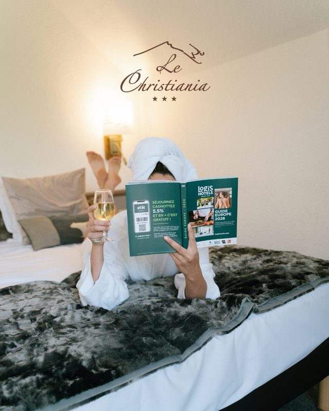 Une cliente en peignoir lit le guide Logis Hôtels, verre à la main, sous le logo du Christiania