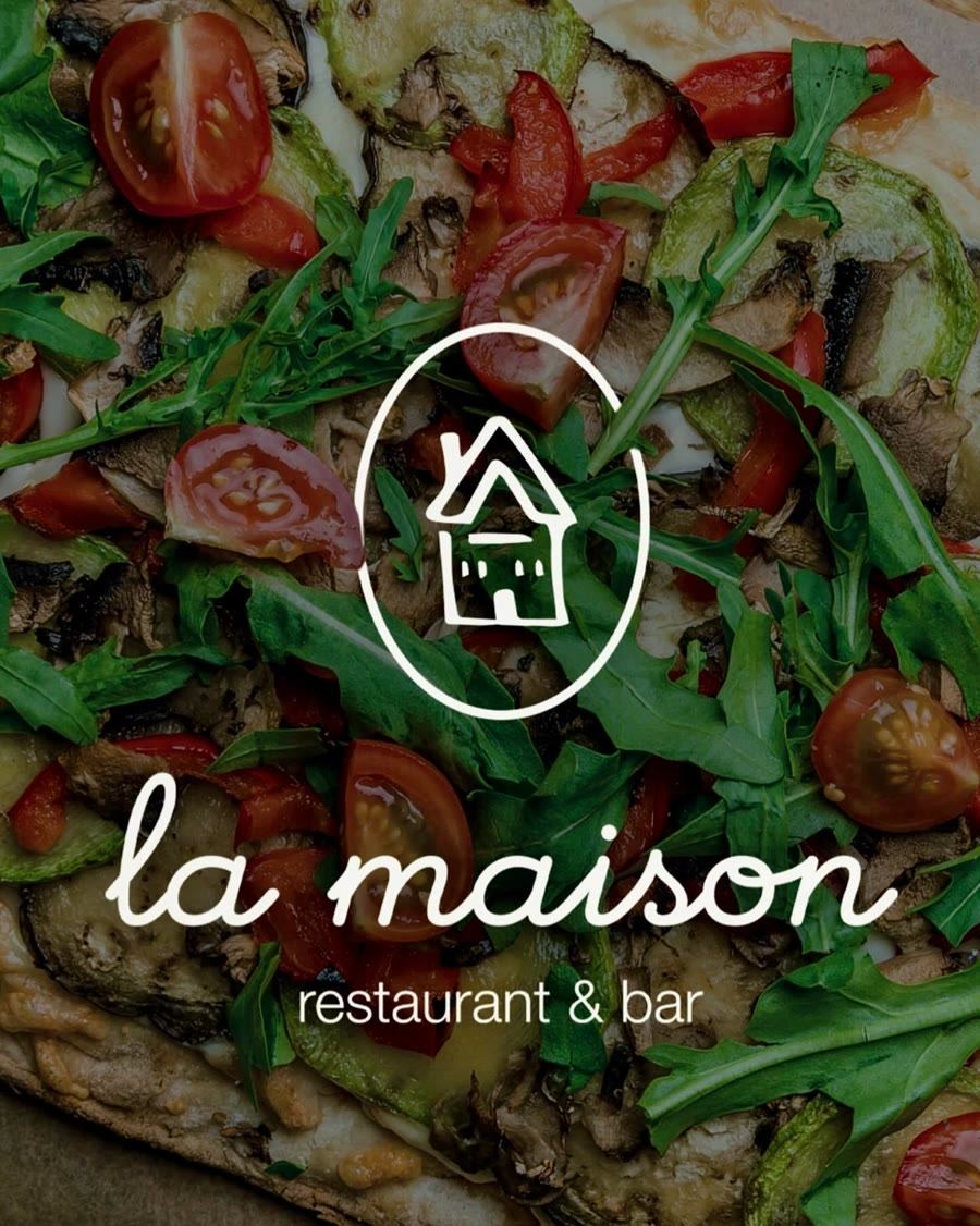Le logo de La Maison, restaurant et bar, dessiné en blanc sur une pinsa aux légumes