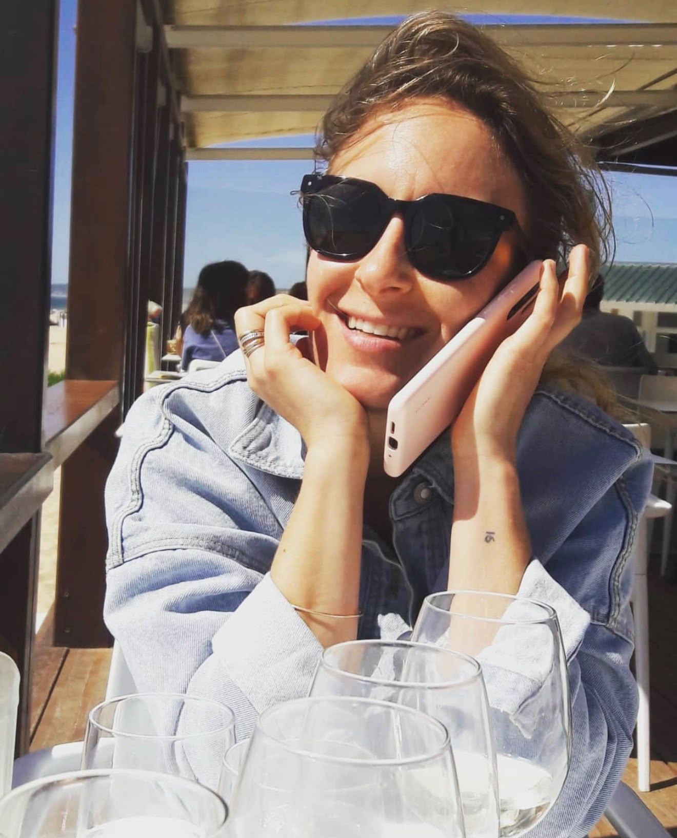 Laure au téléphone en terrasse, lunettes de soleil, le sourire aux lèvres