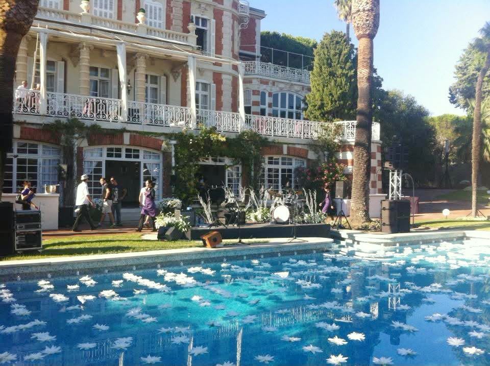La piscine d’un hôtel couverte de fleurs blanches, devant une grande façade de brique et de pierre
