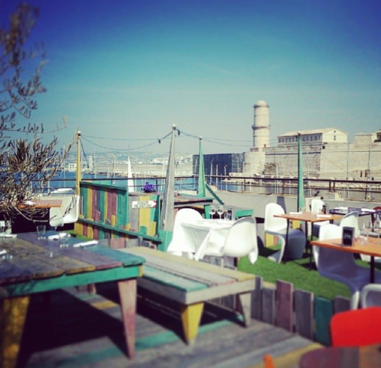 Une terrasse sur les toits de Marseille, tables en bois face au fort Saint-Jean