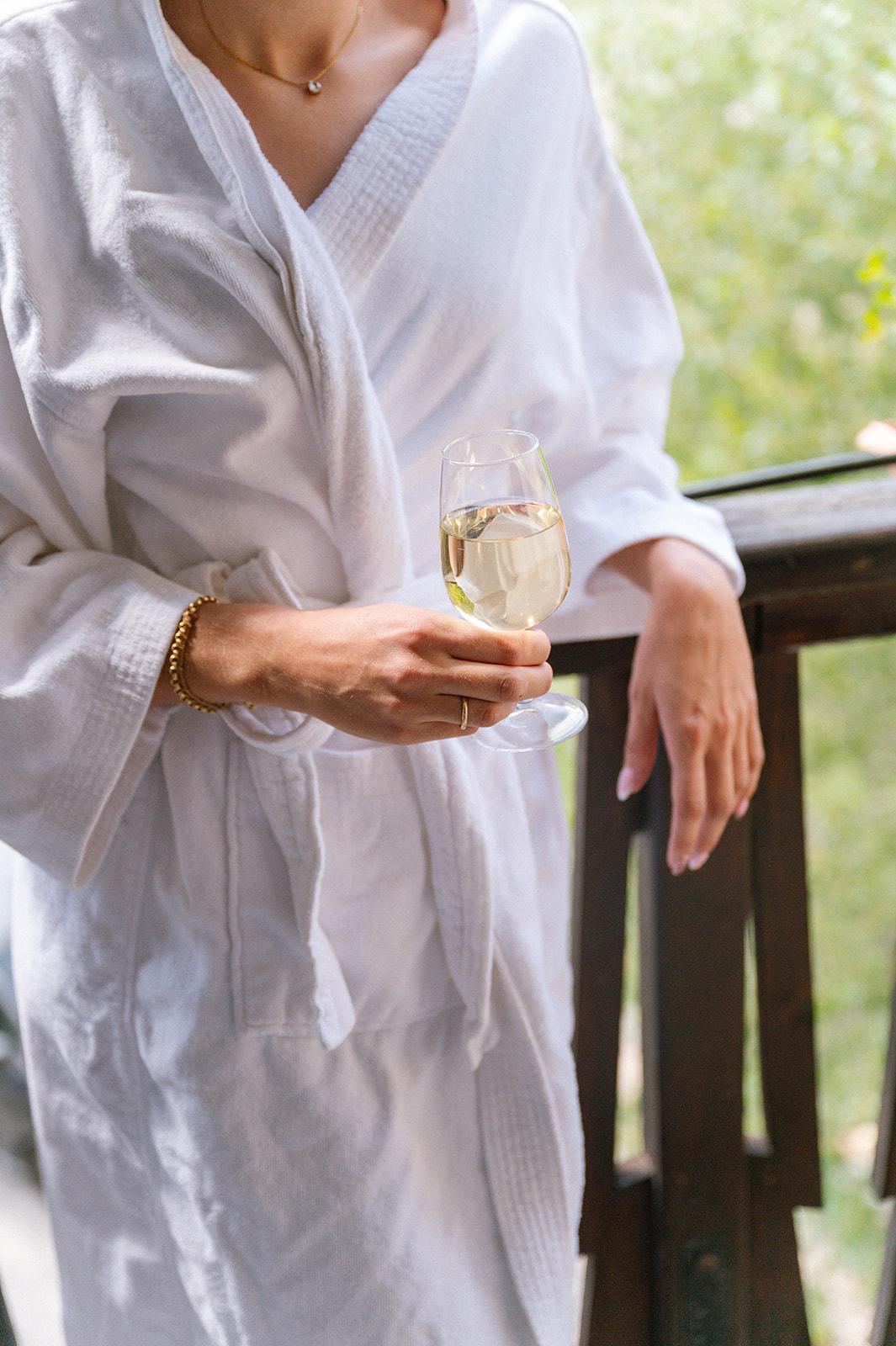 Une cliente en peignoir blanc, un verre de vin blanc à la main, accoudée à un balcon en bois