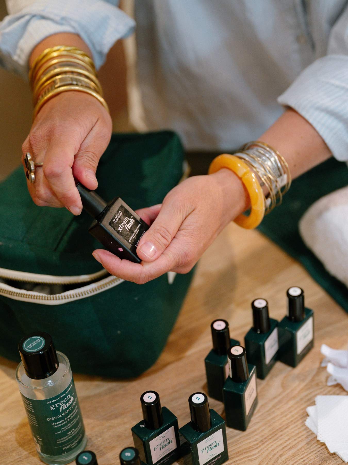 Une manucure Manucurist : une main aux bracelets dorés ouvre un flacon de vernis vert devant la trousse