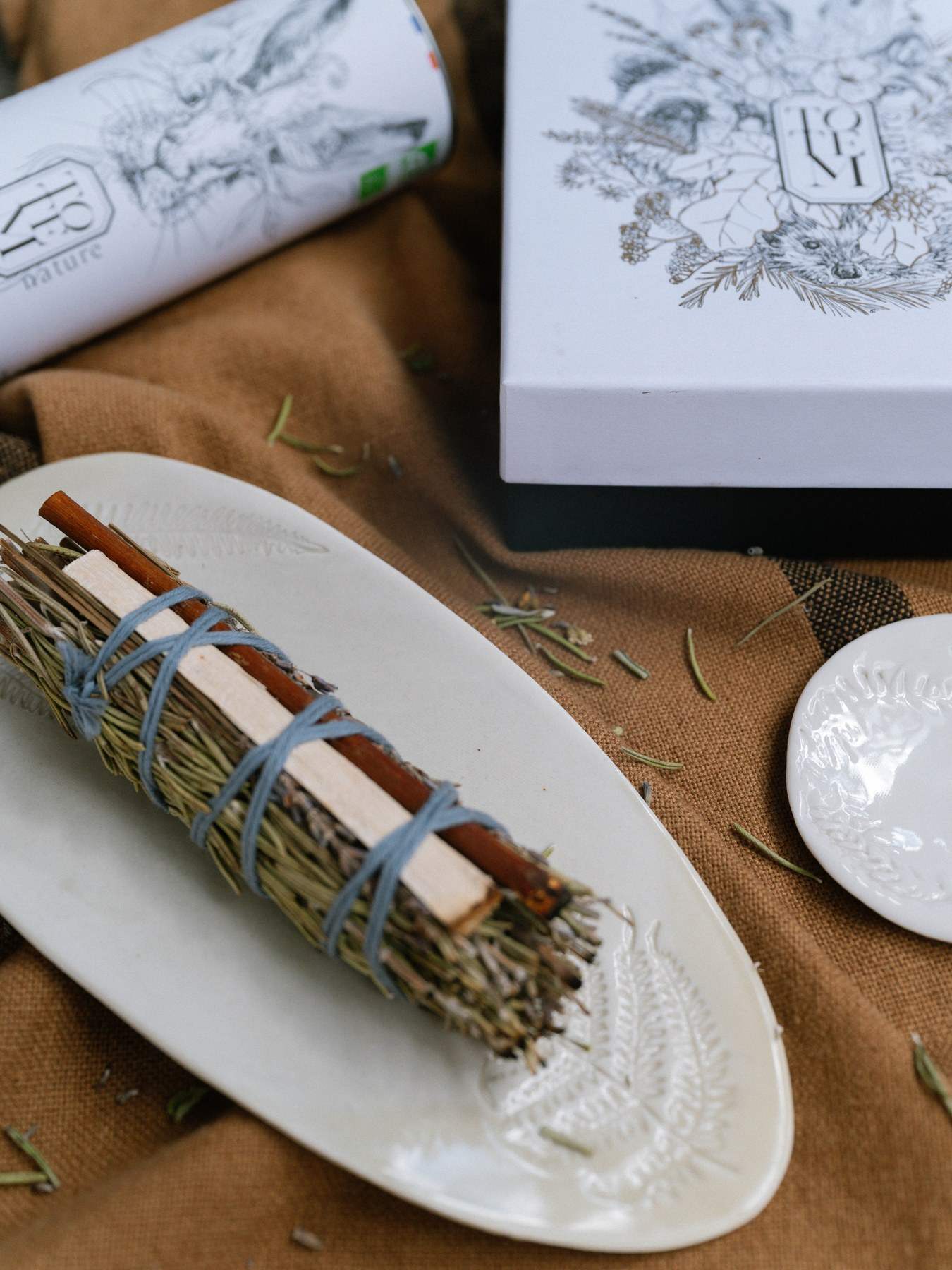 TOTEM, un rituel pour la maison : un bâton d’herbes séchées et de cannelle posé sur un plat blanc