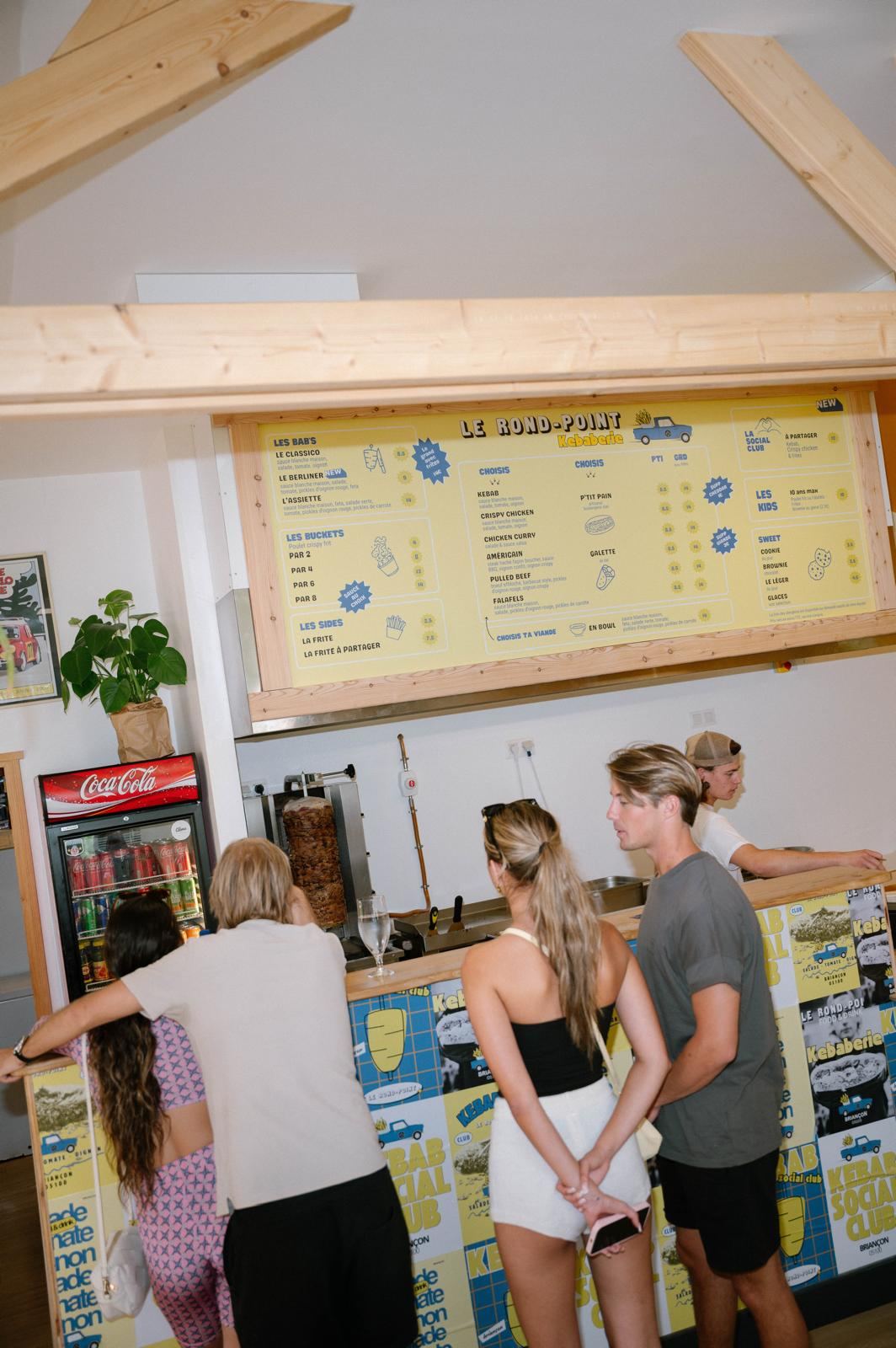 Des clients au comptoir du Rond-Point, sous le grand menu jaune