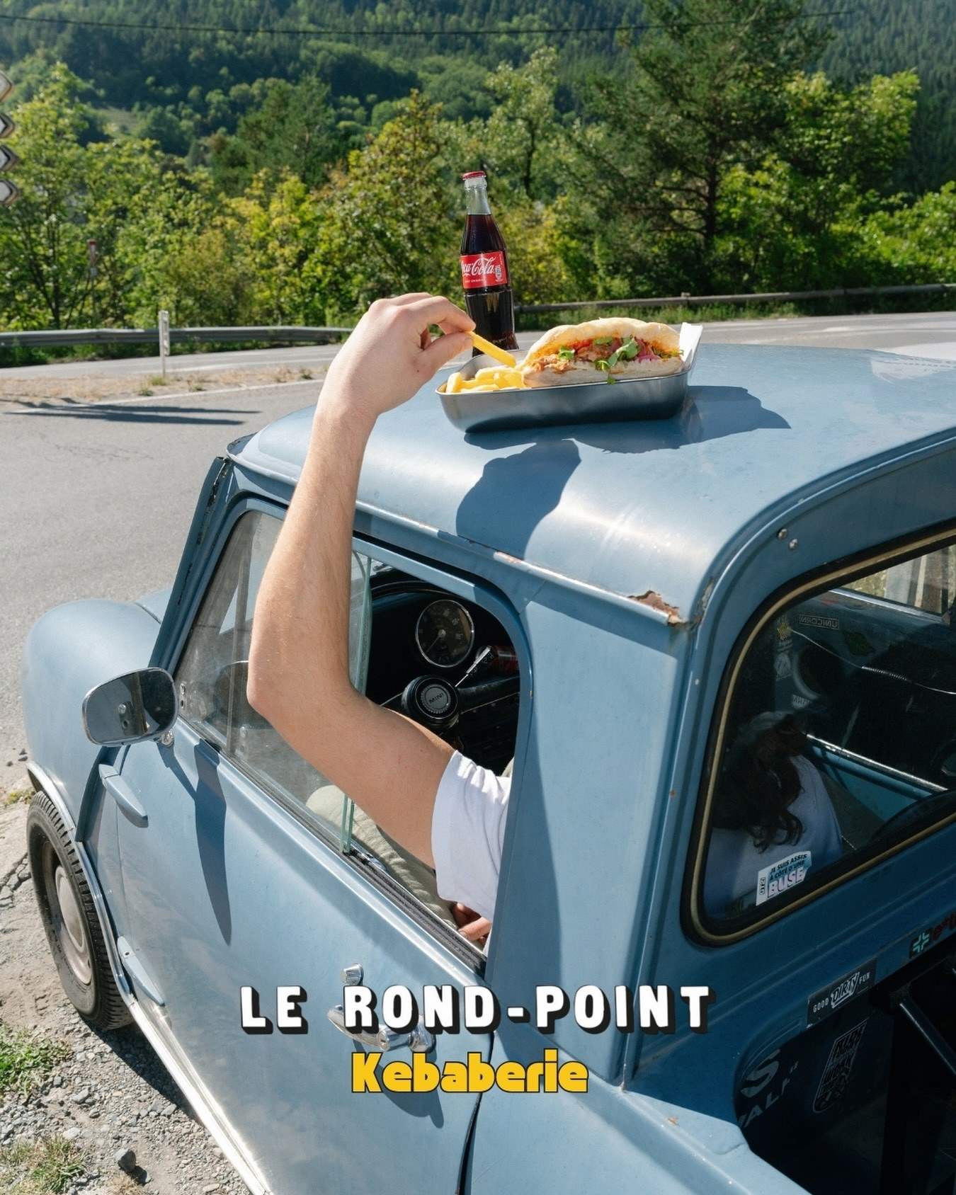 Une barquette de frites et un Coca posés sur le toit d’une vieille voiture bleue : « sur place ou à emporter »