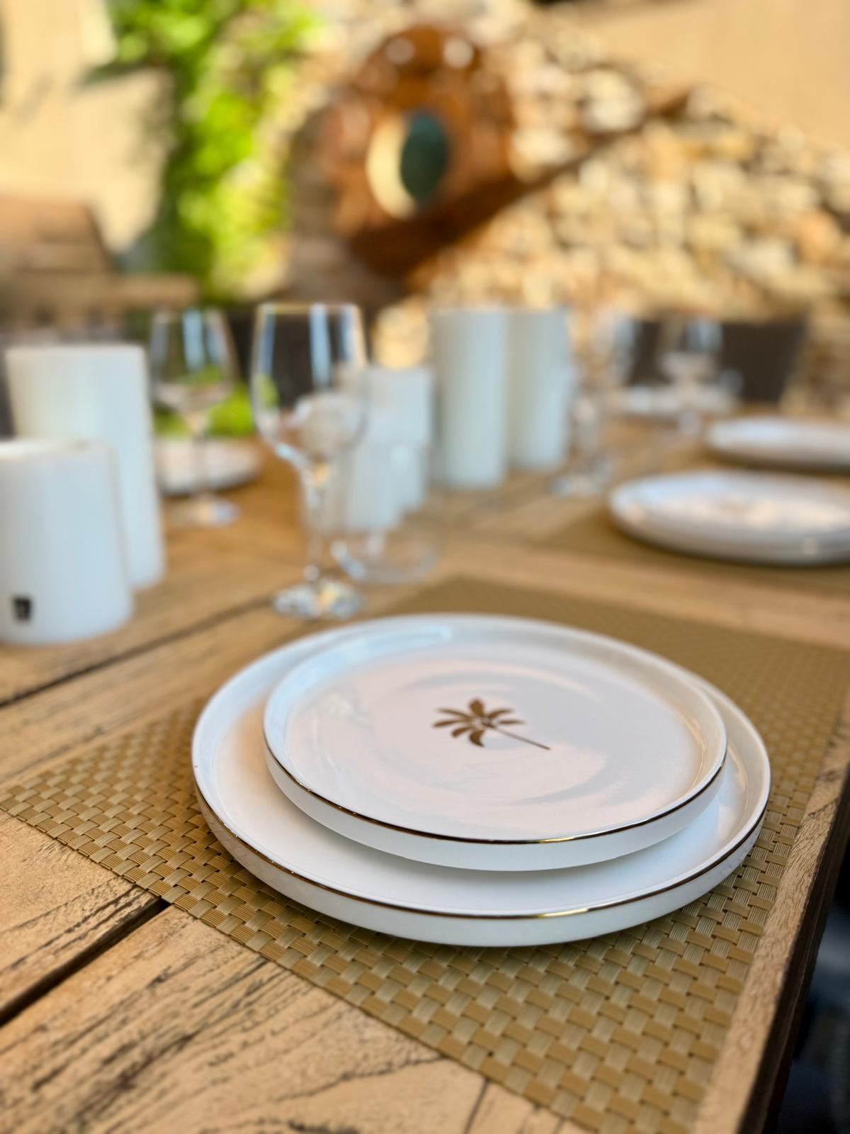 Une assiette blanche au palmier doré posée sur la table, bougies et verres derrière
